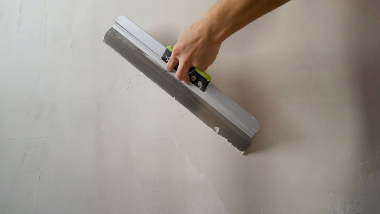 Construction worker smoothing wet plaster on wall using a spatula, during renovation or construction work