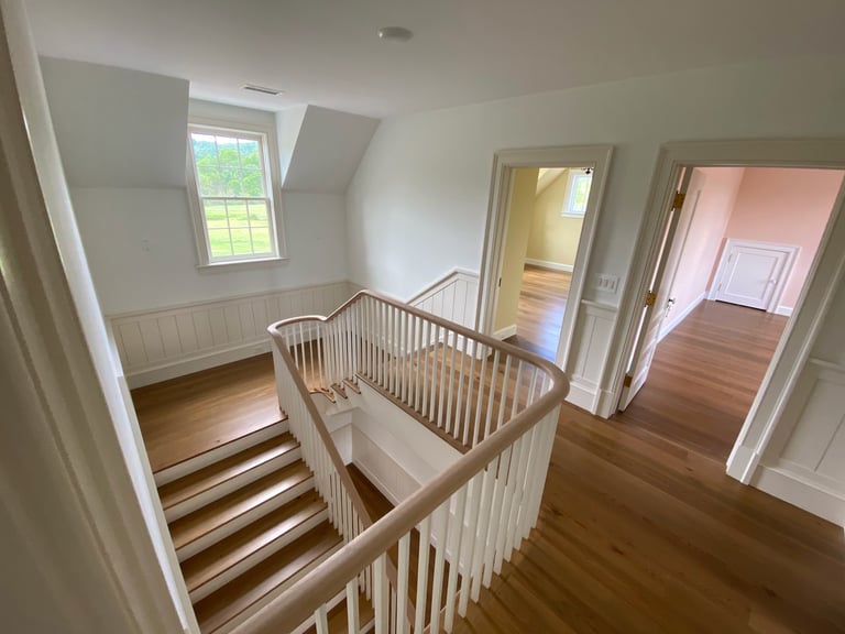 Bright attic hallway with wooden stairs, white railings, skylights, and multiple doorways to adjoining rooms