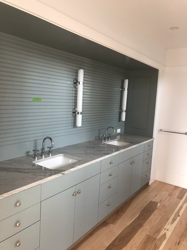 Modern bathroom vanity with dual sinks, white cabinetry, gray tile backsplash, and chrome fixtures under bright mirrors