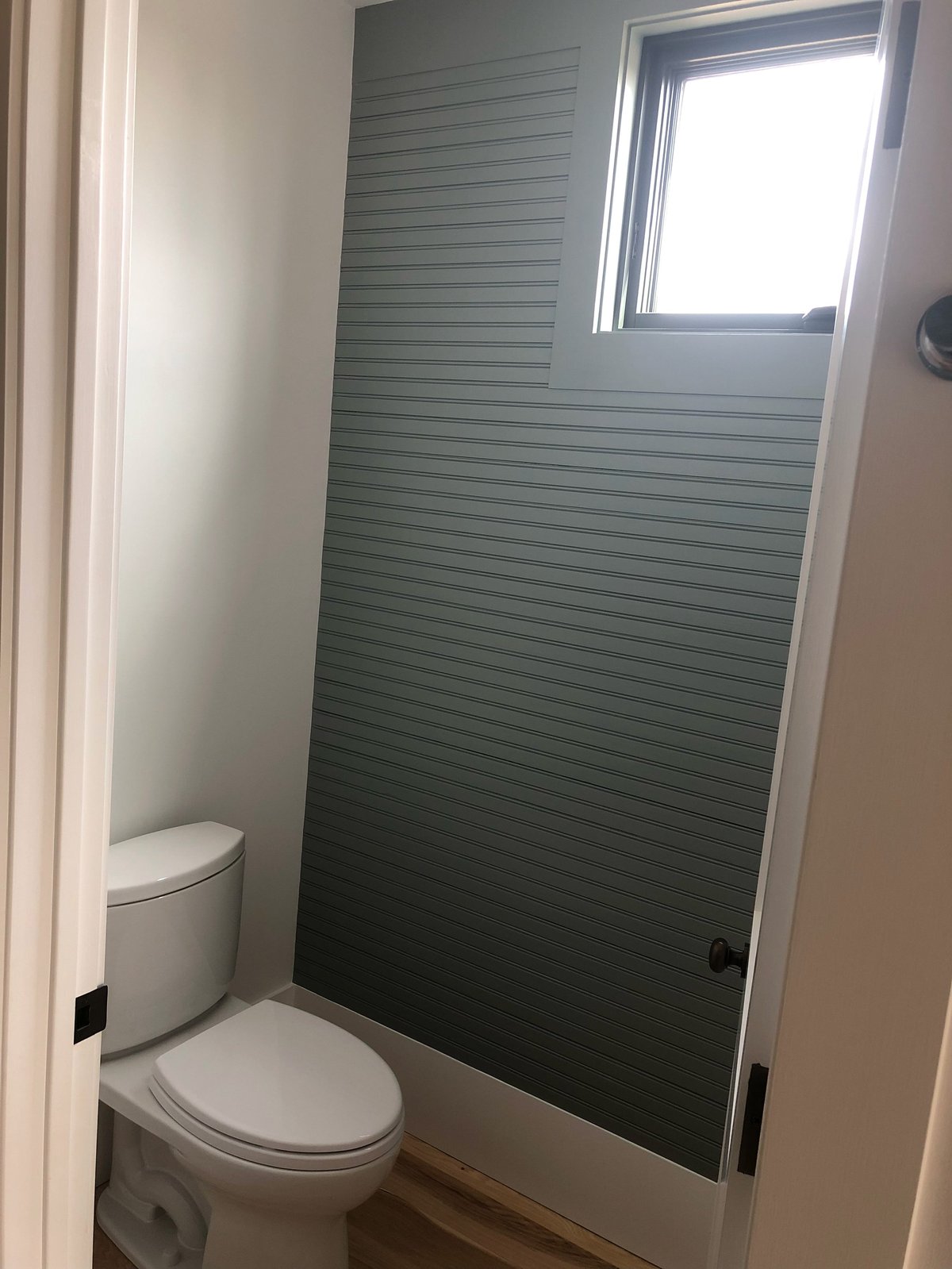 Modern bathroom with white toilet, green horizontal slatted shower enclosure with glass door